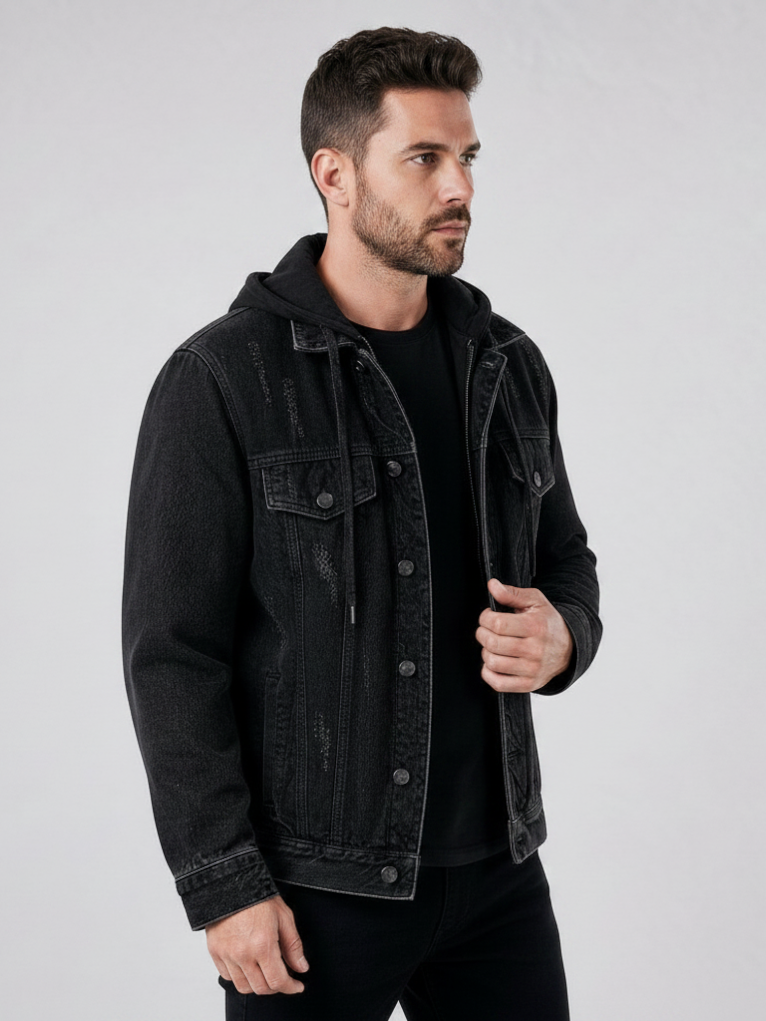 Modelo veste jaqueta jeans preta Habitat Masculino estilo trucker com capuz, lavagem desgastada e detalhes rasgados.