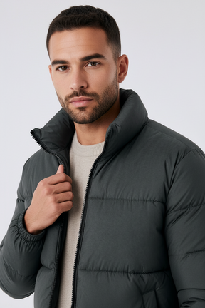 Homem vestindo jaqueta puffer cinza Habitat Masculino com gola alta e zíper frontal sobre malha de tom neutro.