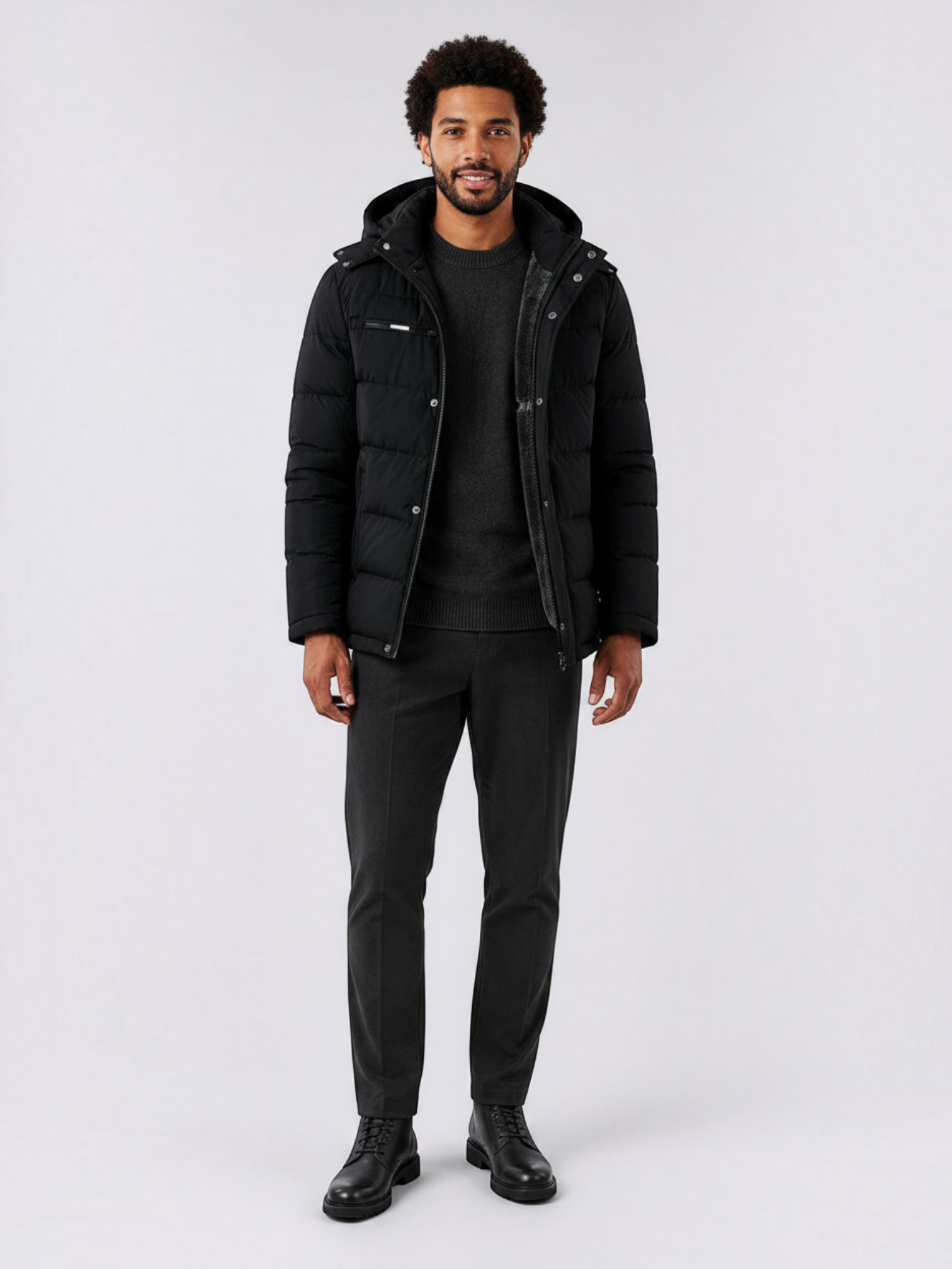 Modelo veste jaqueta puffer preta Habitat Masculino com capuz removível, forro de lã e zíper, sobre suéter e calça social.