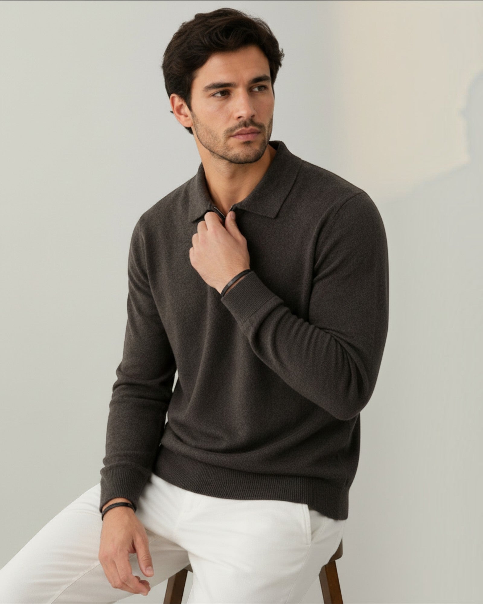Modelo vestindo suéter de lã cinza escuro Habitat Masculino com gola polo e zíper, sentado em estúdio.